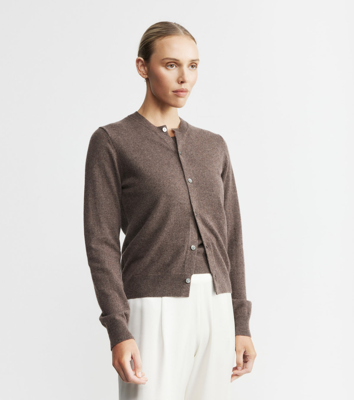 Woman wearing a brown cardigan over a white top on a light gray background