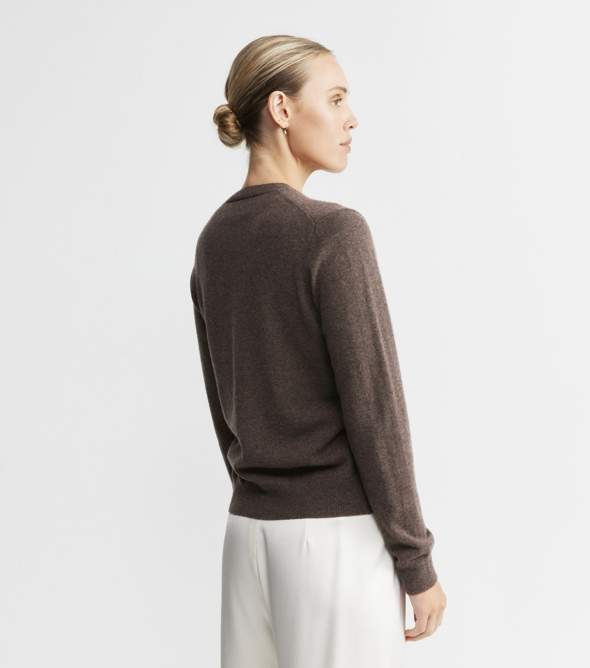 Woman wearing a brown sweater and white pants on a light gray background