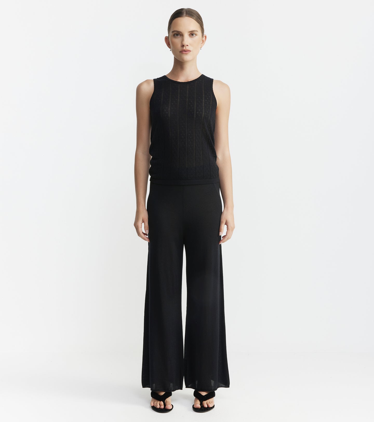 Woman wearing a black sleeveless top and wide-leg pants on a white background